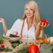 Healthy lifestyle concept with woman holding tomatoes and surrounded by fresh vegetables in a studio setting.